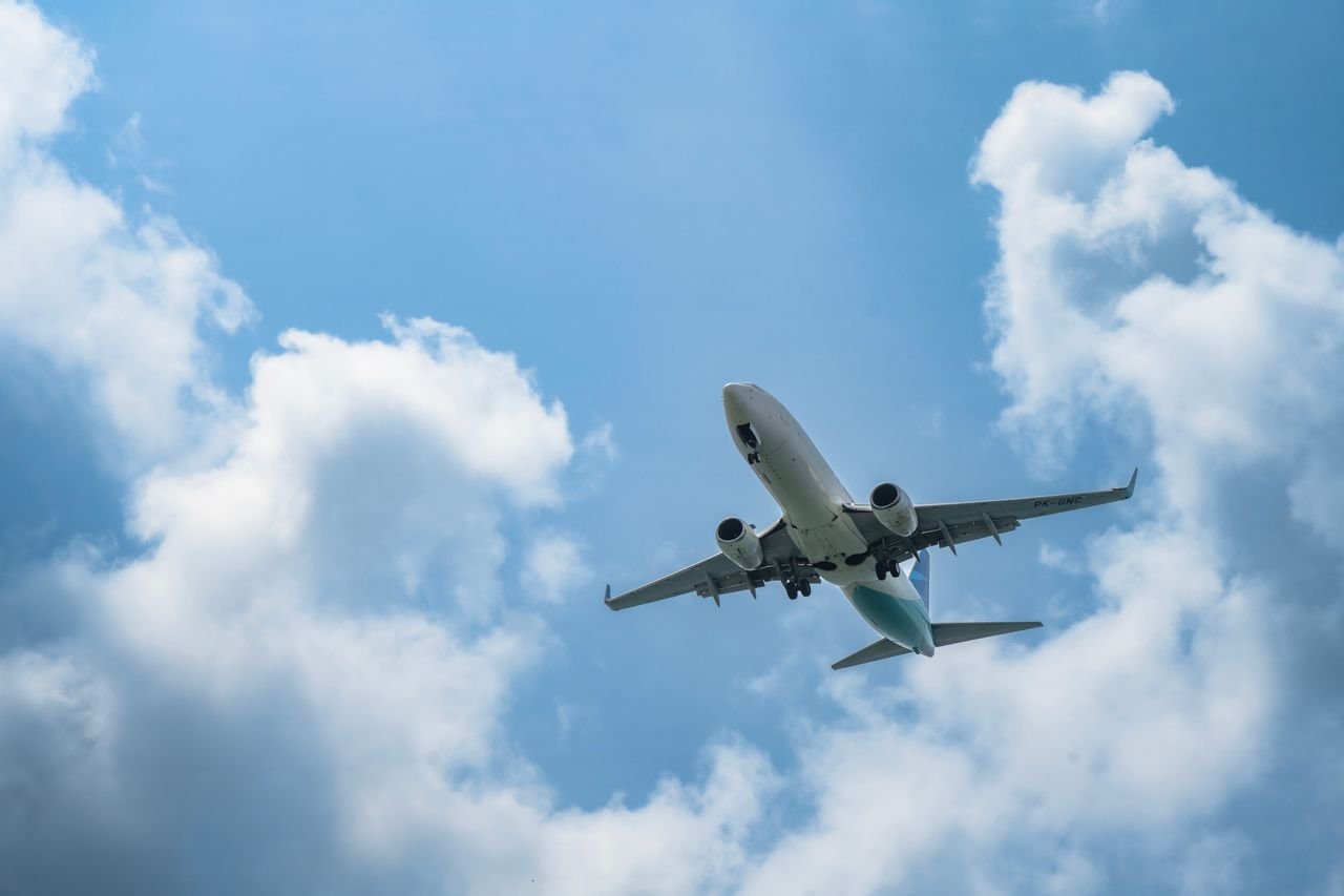 A commercial airplane soars in the sky with white clouds and blue backdrop, ideal for travel concepts.